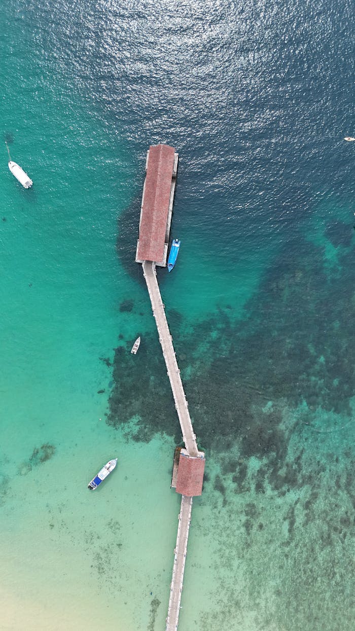 Aerial shot of a wooden pier stretching into turquoise ocean with boats around.